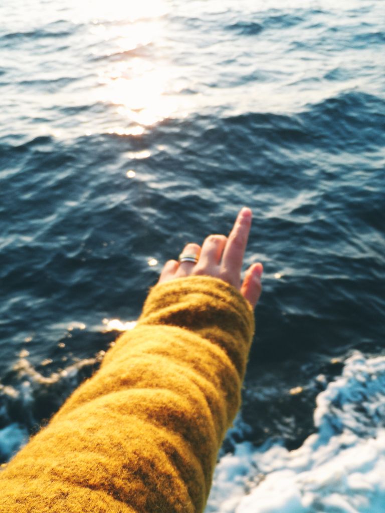 Arm in een okergele wollen trui boven het water